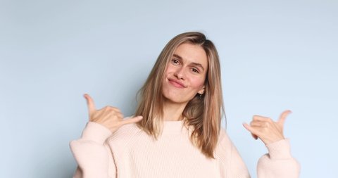Friendly looking positive straight hair woman blonde haircut shows shaka sign gestures indoor being in high spirit, wears fashionable sweater isolated on blue background. Girl show hi or hello gesture