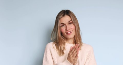 Pretentious blonde straight hair woman in sweater clapping, and looking annoyed over blue background. Girl applauds with a grin, sarcasm sarcastically clapping her hands.