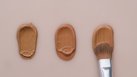 Smearing foundation tones on beige background. Brown cream texture close-up, using brush. Makeup and beauty products concept, cosmetics, eyeshadow palette, bronzer or concealer.
