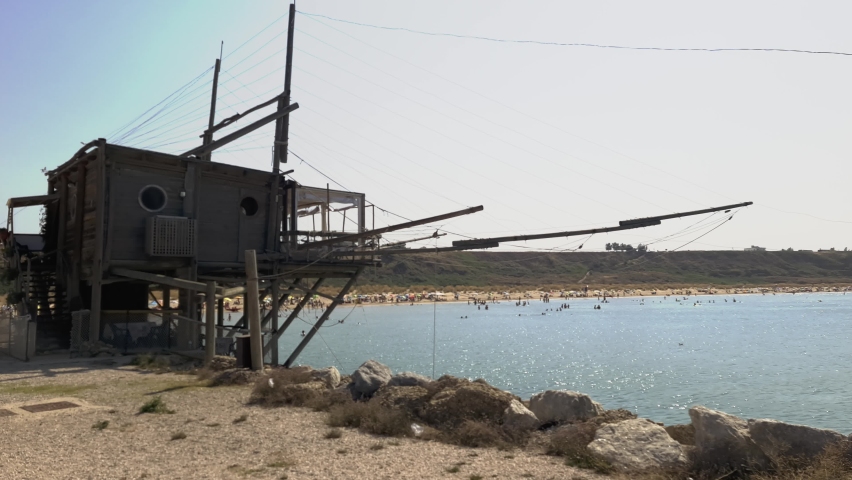 Traditional restaurant in Trabucco fishing house at Punta Penna reserve beach and people bathing in Abruzzo, Italy. Slow-motion