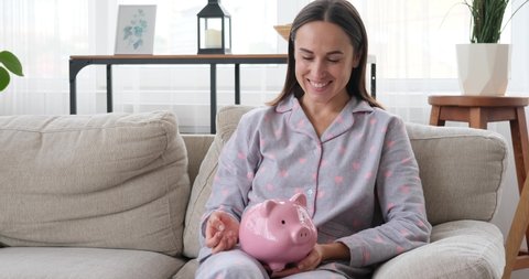 Smiling woman inserting coin into piggy bank