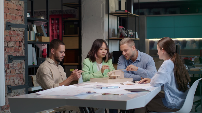 Architects and asian designer working on town area layout in modern office. Diverse group of creative people at table talking and discussing houses design. Co-workers look at model projection of homes | Shutterstock HD Video #1081109735