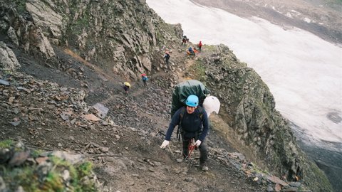 The climber climbs up the mountain with a backpack with equipment, fastened with a carabiner with a belay to the rope. A man climbs up to the top of the mountain