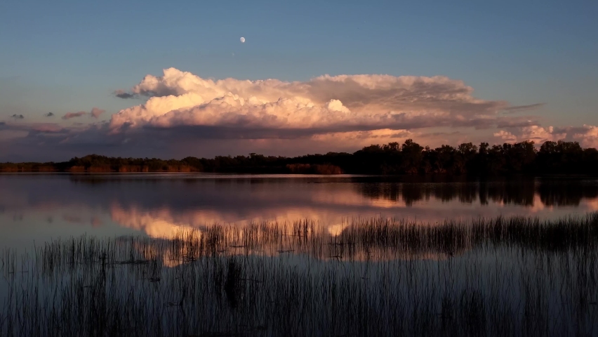 Moonrise over colorful clouds reflected in calm water of Nine Mile Pond in Everglades National Park, Florida at sunset 4K.