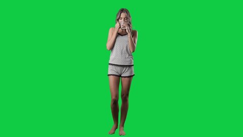 Cute happy woman in pajamas enjoying drinking coffee or tea. Full body isolated on green screen background
