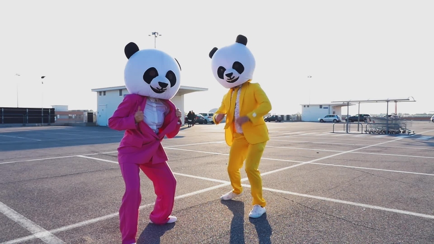 Happy couple wearing a panda giant head dancing and having fun in a parking lot. Man and woman with colored suit going crazy outdoor. | Shutterstock HD Video #1081131725