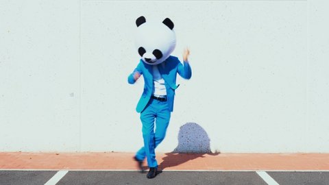 Happy man wearing a giant panda head dancing in a parking lot and having fun