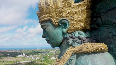 Close up view of Garuda Wisnu Kencana statue in park in Bali, Indonesia, rising above the city. Aerial retreating reveal of large blue and green statue of Hindu religion