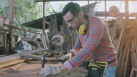 Carpenter woodworker craft man wearing safety glass and earmuff working in furniture shop using professional circular saw machine and glider wood machine blowing saw dust and alignment

