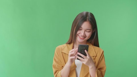 Happy Young Asian Woman Use Mobile Phone While Standing On Green Screen In The Studio
