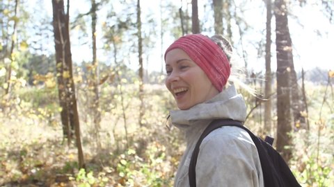 Buff a woman with tied hair on her head. A beautiful white woman with a headscarf was walking in the autumn forest at sunset. The sun shines on a woman on top of a forest walk