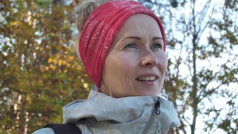 Buff a woman with tied hair on her head. A beautiful white woman with a headscarf was walking in the autumn forest at sunset. The sun shines on a woman on top of a forest walk