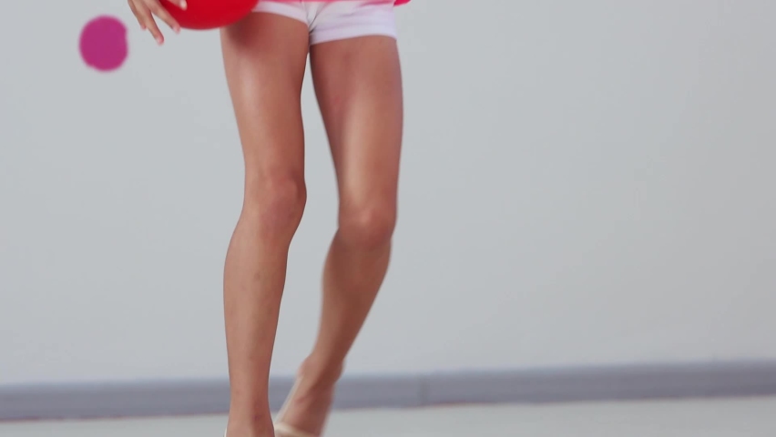 A girl gymnast holding red ball on training while others running around the sports hall