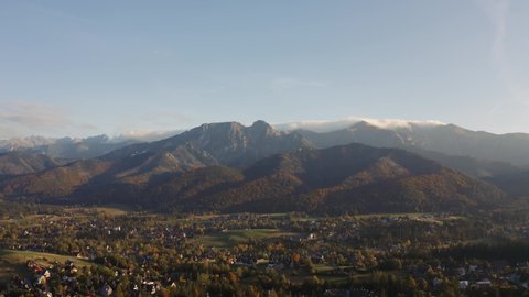Aerial view flight over mountain village lit with evening sunlight. Drone shot beautiful highland valley in sunset light. Picturesque Tatras mountains range covered with clouds, Poland, Zakopane