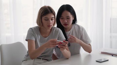 Phone dependency. Gaming nerd. Gadget entertainment. Teen friendship. Excited mixed race girls best friends playing game on smartphone at light home interior.