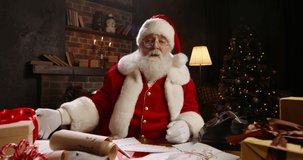 Santa Claus holding New Year present close-up. Talking on video call, using virtual conference, congratulating online, showing gift. Grey-haired Saint Nicholas working at night on Christmas Eve. 