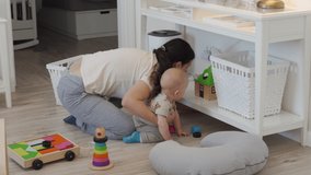 Mother and baby cleaning up toys together on the floor after playing, mom teaches her child to tidying up toys at home. High quality 4k footage