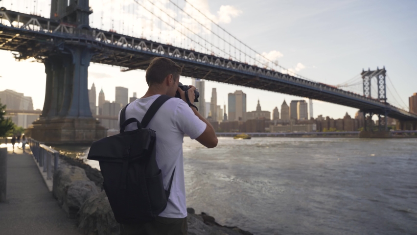 Back of young man photographer with camera, tripod setting up outside outdoors in NYC New York City Brooklyn Bridge Park by east river, railing, looking at view of cityscape skyline Royalty-Free Stock Footage #1081154138