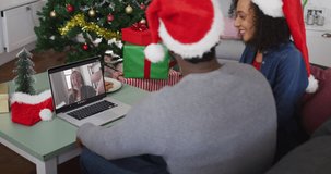 Happy african american couple on video call on laptop with female friend with face mask at christmas. christmas, festivity and communication technology during coronavirus covid 19 pandemic.