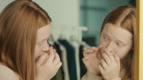 A Red Haired Teenage Girl Examines Her Reflection in the Mirror. Adolescence Concept, Mental and Emotional Health. Body Positive. Mental Health.