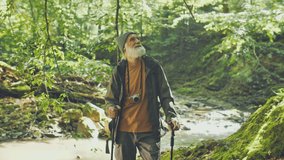 Happy Elderly Man with a Backpack and Nordic Walking Sticks Standing Near the River Enjoying Nature While Hiking in the Forest. Active Retirement, Tourism and Hobby Concept.