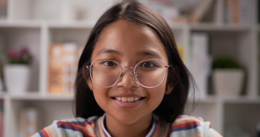 Closeup of Young asian active girl glasses looking at camera while sitting at desk at classroom. Education concept.