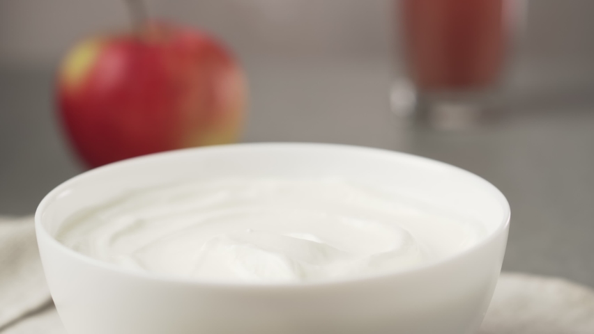 Hand picks up yogurt with a spoon. Bowl of greek yogurt with apple and glass of juice.  Royalty-Free Stock Footage #1081161185