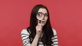 Portrait of woman looks into camera through magnifying glass, inspects something, private detective, wearing casual style long sleeve shirt. Indoor studio shot isolated on red background. - Powered by Shutterstock - Get 15% off with code: PIKWIZARD15