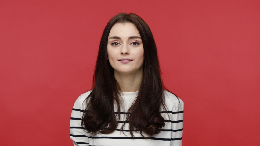 Portrait of playful woman covering eyes with heart shape lollipops, having positive expression, wearing casual style long sleeve shirt. Indoor studio shot isolated on red background.
