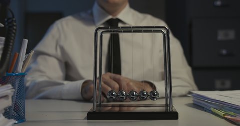 Sad office worker sitting at desk and staring at Newton's cradle balls