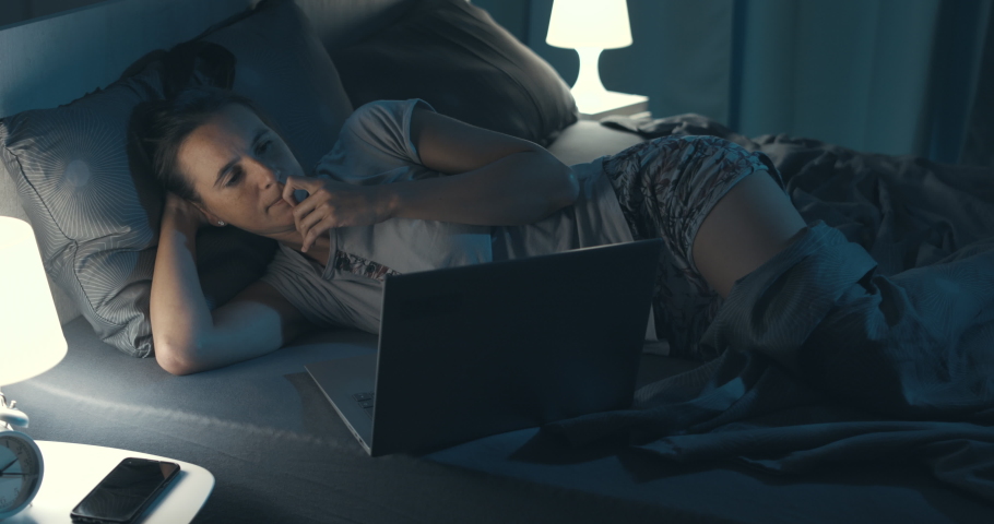 Woman lying in bed and connecting with her laptop late at night, she can't sleep | Shutterstock HD Video #1081171340