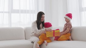 Little kids in red Santa hat giving a Christmas gift for their mother at home