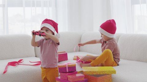 The Season of Giving concept. Two kids in Santa hat are opening Christmas gift boxes, playing at home Winter time, New Year presents and seasonal tradition - gift-giving.