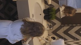 Vertical Video. Little Girl in White Bathrobe Drying her Hair in the Bath of Hotel Room or Apartment. People, Lifestyle and Daily Routine Concept