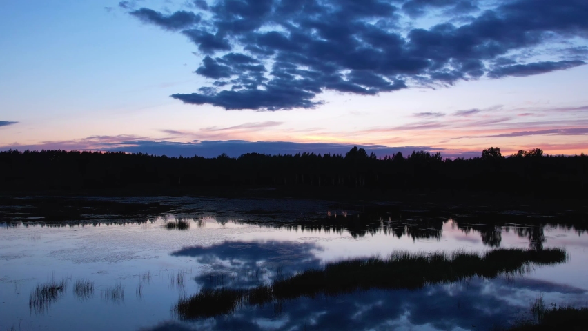flight in the evening over the calm water of a forest lake. sunset behind the black silhouette of the forest