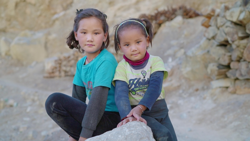 shot of two cute and adorable young little countryside Asian girls sitting together on a rock looking at the camera during morning daylight