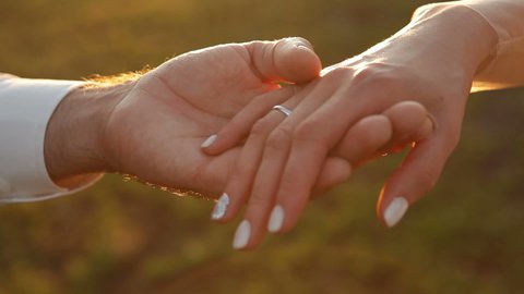 A man and a woman hold hands, against the backdrop of the sunset. The groom holds the bride hand. Two lovers joined hands.
