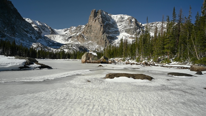 Hiker walking on a frozen body of water named Two Rivers Lake with Notchtop Mountain in the background, Fall, Rocky Mountain National Park, Colorado, USA