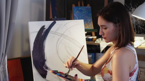 Artwork painting. Woman artist. Art therapy. Creative lifestyle. Talented female painter drawing with paintbrush acrylic paint at canvas on easel in studio workshop interior.
