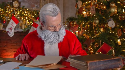 Santa Claus (Father Christmas, Kriss Kringle) opening a letter from a child with wishes for the New Year. A handsome old wizard carefully reading a message from a child. A scene from a fairy tale