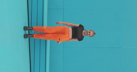 Vertical video of dancing happy girl moving with rhythm of music in sportswear on blue background, contemporary dance