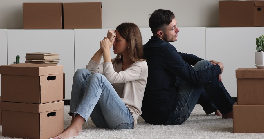 Stressed young family couple sitting on floor carpet between big carton boxes, feeling disappointed with real estate purchase, having problems with moving into new apartment, tired of long relocation. Royalty-Free Stock Footage #1081201358