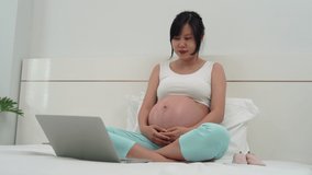 Social communication concept.Pregnant woman taking a video conference with her husband. A pregnant woman is waving to her husband and showing the pink shoes prepared for her daughter. 