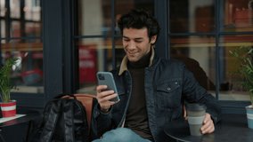 Young arabian traveler using smartphone and drinking coffee while sitting on cozy cafe terrace. Handsome guy with backpack visiting new places during vacation. - Powered by Shutterstock - Get 15% off with code: PIKWIZARD15
