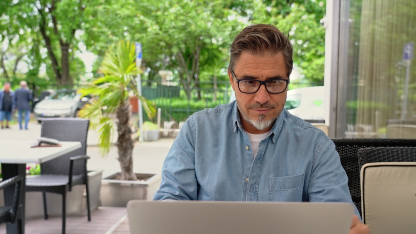 Outdoor portrait of mid adult man in 50s, happy confident smile. Working with laptop computer. Mature age, middle age, bearded, glasses. Royalty-Free Stock Footage #1081209722