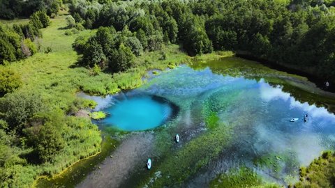 Bird's-eye view of a forest lake. Sup tour of many vacationers on a hot summer sunny day. The deep karst gaps of lake are filled with blue water. Pure clear water glistens in sun's rays. Drone footage
