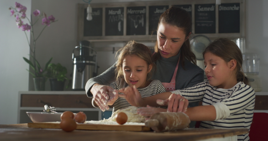 Portrait of Woman and Daughters in the Kitchen Baking Together. Mother Teaching her Little Girls How to Make Dough. Two Sisters Helping Their Mother with Cooking, Learning a New Skill Royalty-Free Stock Footage #1081210613
