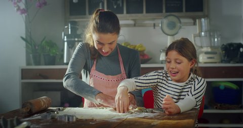 Cinematic authentic shot of happy mother and little daughter are having fun to make forms on dough together for baking cookies in kitchen at home.