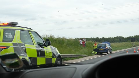 MOTORWAY M5, ENGLAND, UNITED KINGDOM - CIRCA JUNE, 2021: Driving M5 highway past broken down car and people on roadside. Traffic officer is present with marked car and flashing lights.