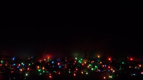 Flat lay glowing Christmas lights with copy space on dark plank background. Shot in 4k resolution. Multicolored Abstract Bokeh Background. Festive background with space for text. 